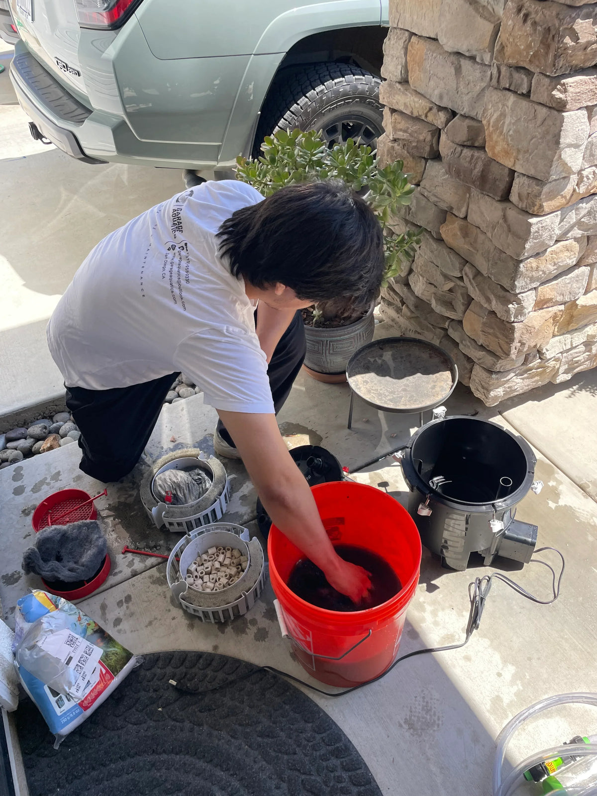 A person preparing aquarium equipment and water in a red bucket outdoors.